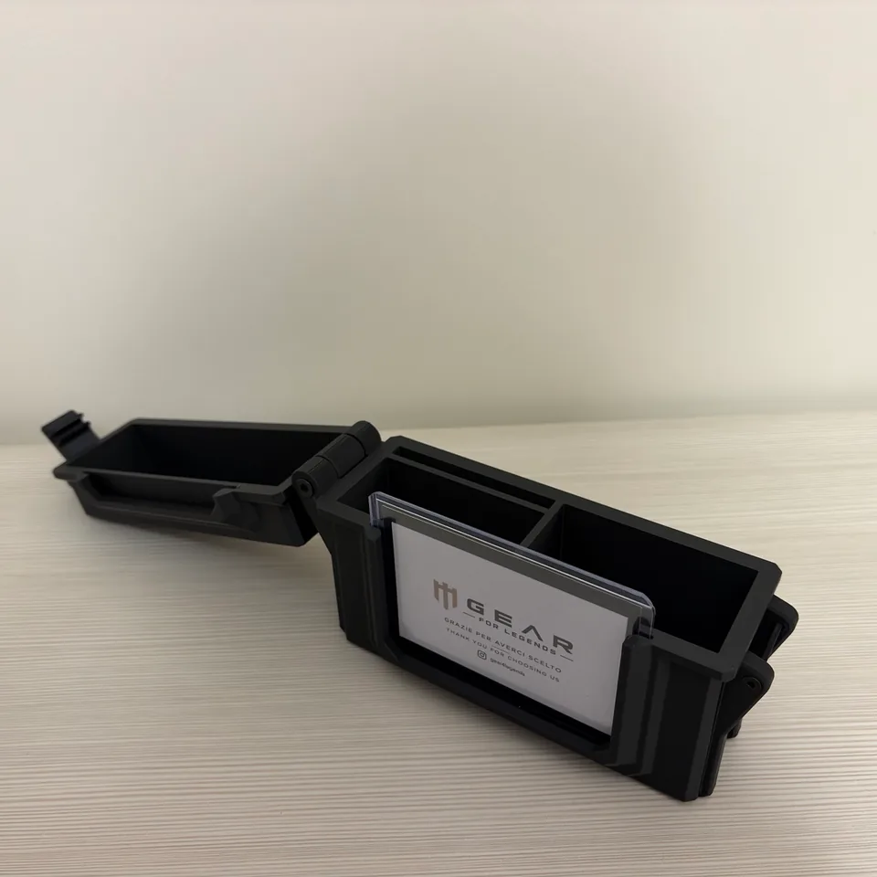 Aegis nera aperta su un piano chiaro, vista di lato: il coperchio incernierato è ribaltato a sinistra e la base mostra gli scomparti interni; sul fronte si vede il cartoncino con il logo Gear For Legends.